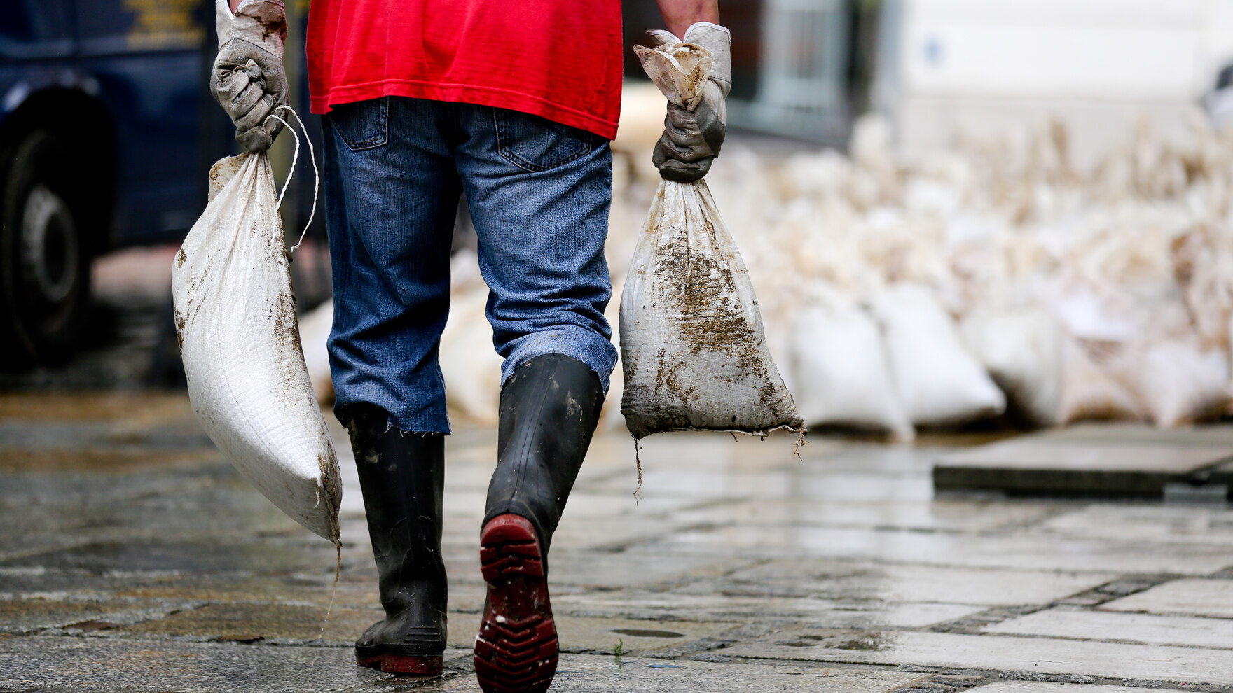 Mann mit Sandsäcken in der Hand und Gummistiefeln läuft